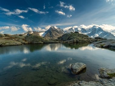 Glasklarer Bergsee mit Blick auf Schneegipfel bei einem fantastischen Wolkenspiel.