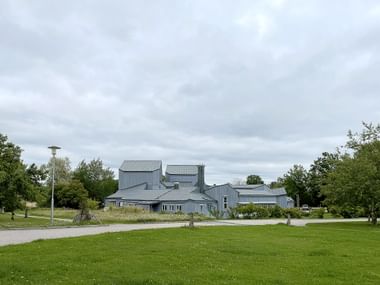 Moderner grauer Metallgebäudekomplex des Kulturhuset Ytterjärna, umgeben von grünen Rasenflächen und Bäumen unter bewölktem Himmel.