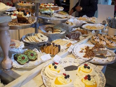 Reichhaltiges schwedisches Kuchenbuffet mit verschiedenen Gebäcken, Kuchen und Keksen auf Etageren und Tellern, darunter Desserts mit Sahne.