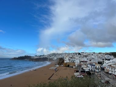 Küstenansicht von Albufeira mit weißen Häusern am Hang, Sandstrand und Atlantik unter blauem Himmel mit Wolken.