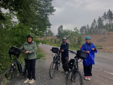 Drei Radfahrer mit Tourenrädern und Packtaschen auf einer Waldstraße unter bewölktem Himmel bei Mariefred, Schweden.