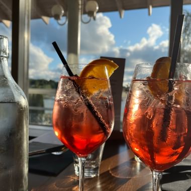 Zwei Apérogläser mit Apérol Spritz und eine gefüllte Wasserflasche stehen auf einem Tisch.