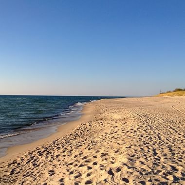 Links der Blick zum offenen Meer der übergeht zum Sandstrand in Litauen, der mit Fussabdrücken übersäht ist und bis zum Horizont, zum sonnigen Himmel führt.