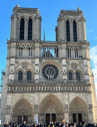 Westfassade der Kathedrale Notre-Dame in Paris mit Zwillingstürmen, Rosette und gotischen Bögen. Besucher versammeln sich am Eingang.