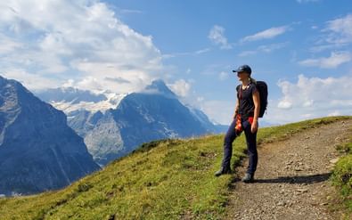 Wanderin steht auf Bergweg und schaut zur grossen Scheidegg.