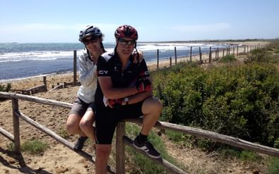 Die zwei Radfahrer sitzen auf einem Holzzaun vor der Meeresküste von Sizilien.