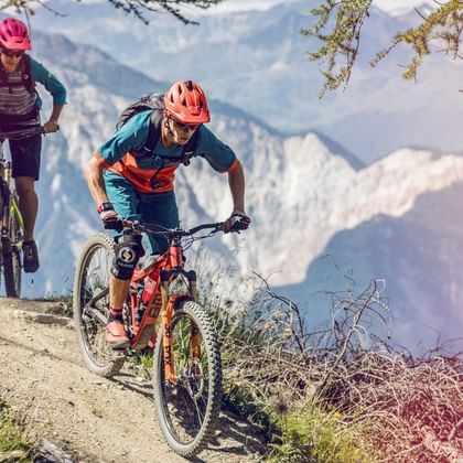 Zwei Mountainbiker fahren auf einem Weg mit Aussicht auf die Berge in Loèche-les-Bains.