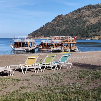 Drei Liegestühle stehen am Strand und im Meer befinden sich drei Holzboote