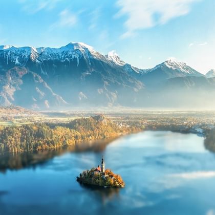 Eine Insel, mitten im See, steht eine Kirche auf einer Insel. Der Wald und der Berg im Hintergrund sind so mächtig, dass die Insel wie eine Miniaturausgabe aussieht.