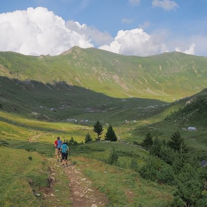 Wanderer auf Bergpfad auf dem Balkan Zwei Wanderer gehen auf einem Erdweg durch ein grünes Bergtal auf dem Balkan mit sanften Hügeln und bewölktem blauen Himmel.