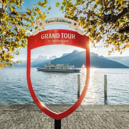 Ein Fotopunkt von Grand Tour Switzerland am Vierwaldstättersee in Brunnen. Im Hintergrund ein Schiff.
