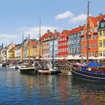 Historischer Nyhavn-Hafen in Kopenhagen mit bunten Bürgerhäusern aus dem 17. Jahrhundert am Kanal und traditionellen Segelschiffen im Wasser.