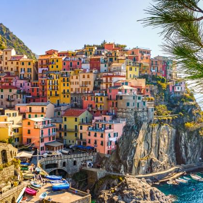 Bunte Häuser auf steilen Klippen in Cinque Terre, Italien. Das Dorf zeigt gelbe, rosa, orange und rote Gebäude, die zu einem kleinen Hafen mit Booten hinabführen.