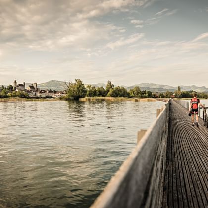 A man crosses a wooden bridge leading into the old town of Rapperswil. Heart route. Cycling holidays with Eurotrek.