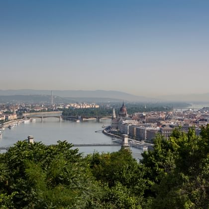 Erhöhte Ansicht von Budapest mit der Donau und Brücken, dem ungarischen Parlamentsgebäude und der Stadtlandschaft unter klarem Himmel.