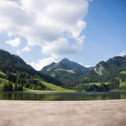 Lac de Schwarzsee avec eau calme reflétant les montagnes alpines vertes et forêts sous un ciel bleu avec nuages blancs dans la région de Fribourg.