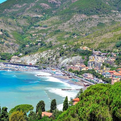 Luftaufnahme von Levanto, Italien mit einem geschwungenen Sandstrand und bunten Gebäuden entlang der Küste, umgeben von grünen Hügeln.
