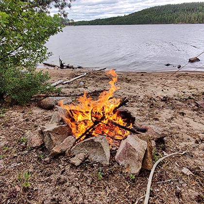 Feuer vor einem See mit Zelt im vordergrund.