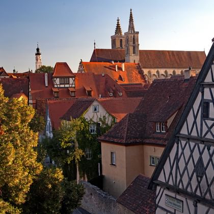 Mittelalterliche Stadtansicht von Rothenburg ob der Tauber mit Fachwerkhäusern, roten Ziegeldächern und gotischen Kirchtürmen unter blauem Himmel.