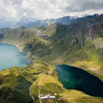 Luftaufnahme des Lago Ritom in den Alpen Vogelperspektive des Lago Ritom, ein dunkelblauer Alpensee umgeben von grünen Bergen und felsigen Gipfeln in den Schweizer Alpen.