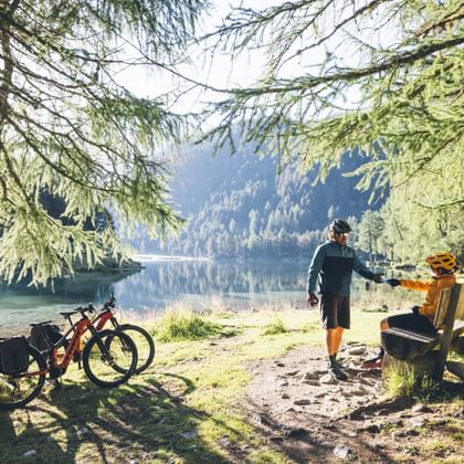 Des cyclistes font une pause sur un banc au bord d'un lac de montagne.