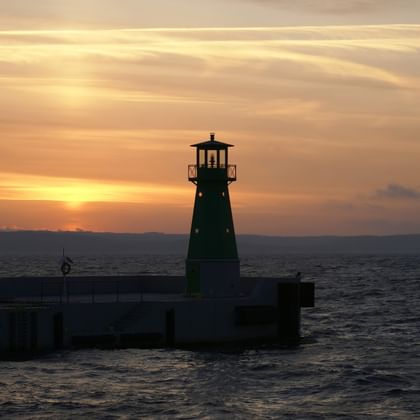 Wunderschöner Sonnenuntergang am Meer mit einem Leuchtturm im Vordergrund. Aktivferien mit Eurotrek.