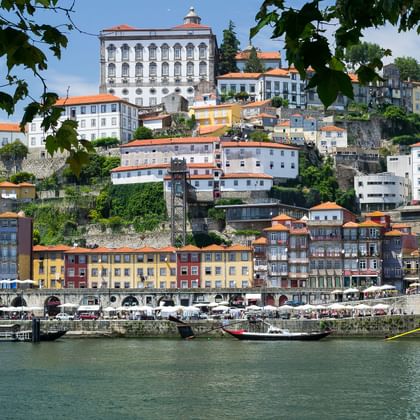 Blick auf Portos historischen Hügel mit bunten Gebäuden entlang des Douro. Traditionelle Boote liegen am Ufer.