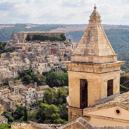 Ragusa Ibla historische Stadt mit Glockenturm Panoramablick auf Ragusa Ibla mit Steinturm im Vordergrund und historischer Hügelstadt mit traditionellen Gebäuden im Hintergrund.