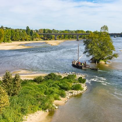 Vue pittoresque de la Loire avec des bancs de sable, un bateau traditionnel en bois et une végétation verte luxuriante le long du dernier fleuve sauvage d'Europe.