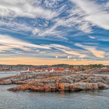 Malerischer Blick auf den Hafen von Sandefjord im Oslofjord mit felsigen Inseln, Wohngebäuden entlang der Küste und dramatischem Wolkenhimmel.