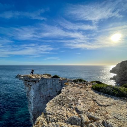 Einsamer Wanderer auf dramatischer weißer Kalksteinklippe bei Ses Piquetes an Mallorcas Ostküste mit Blick auf türkises Mittelmeer unter sonnigem Himmel.