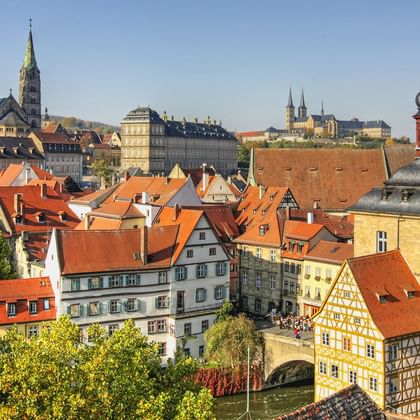 Panoramablick auf Bambergs Altstadt mit roten Ziegeldächern, historischen Fachwerkhäusern, Kirchtürmen und dem Alten Rathaus am Fluss.
