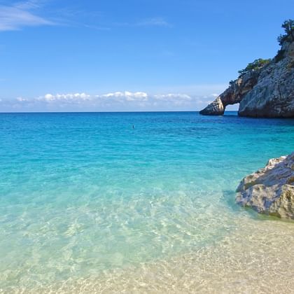 Kristallklares türkisfarbenes Wasser am Strand Cala Goloritze auf Sardinien mit weißen Kalksteinklippen und natürlichem Steinbogen.