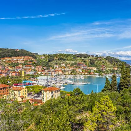 Panoramablick auf La Spezia mit bunten Häusern an Hängen, einem Yachthafen mit Segelbooten und dem blauen Golf von La Spezia unter klarem Himmel.