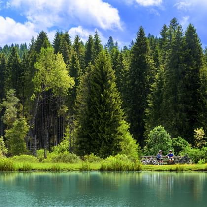 Zwei Fahrradfahrer sitzen an einem See mit einem Wald im Hintergrund