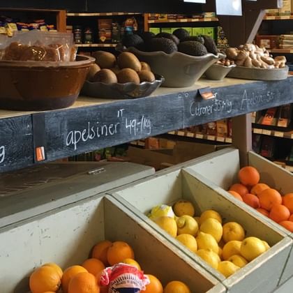 Innenansicht eines Lebensmittelladens in Stockholm mit Obst- und Gemüseauslage, Orangen und Zitronen in Holzkisten sowie Avocados auf Regalen.