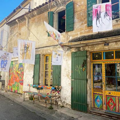 Bunte Kunstgalerie in Provence-Dorf Traditionelles provenzalisches Gebäude mit grünen Fensterläden zeigt bunte Kunstwerke und Gemälde an den Wänden mit Kunstgalerie.