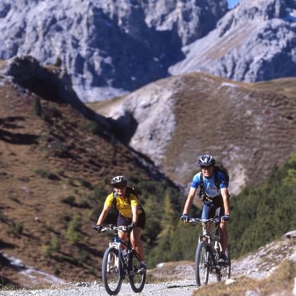 Zwei Mountainbiker auf einem Steiweg. Im Hintergrund die mächtigen Bündner Berge.