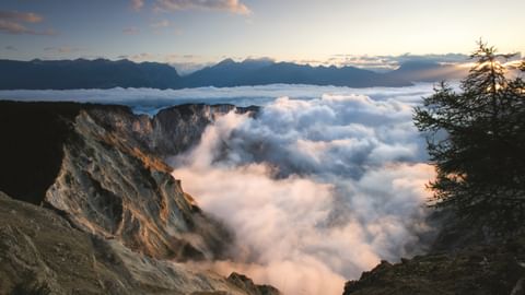 Sonnenuntergang Wolken zwischen Bergen Dramatischer Sonnenuntergang mit dicken Wolken zwischen felsigen Berghängen. Dunkle Bergspitzen über Wolkendecke, Tannen rechts sichtbar.