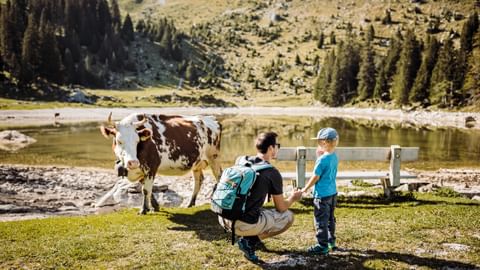 Ein Mann und sein Sohn stehen neben einer Kuh an einem See im Gantrisch Naturpark.