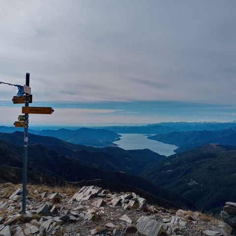 Ein Wegweiser vor einem wolkenbedeckten Bergpanorama. Sentiero Lago di Lugano. Wanderferien mit Eurotrek.