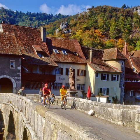 Zwei Velofahrer fahren über eine Brücke in St. Ursanne im Kanton Jura auf ihrer Velotour von Eurotrek von Basel nach Nyon.