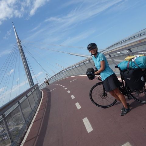 Eine Frau steht mit ihrem Fahrrad auf einer Brücke für Radfahrer.