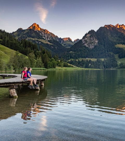 Zwei Wanderer sitzen auf einem Steg am Schwarzsee. 