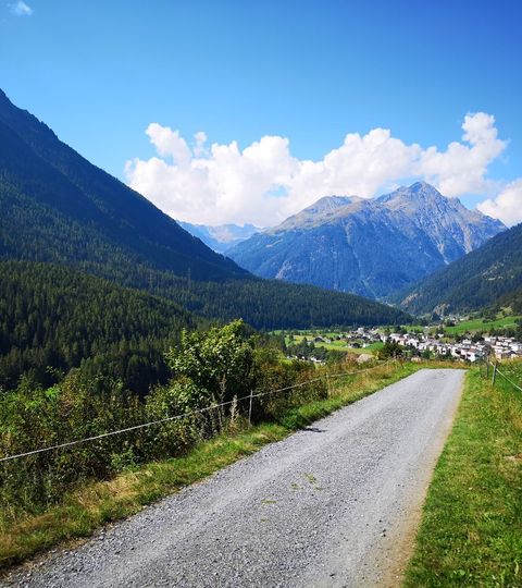 Naturstrasse zwischen Weideland, die direkt zum Dorf führt, welches unter den schönen Bergen liegt.