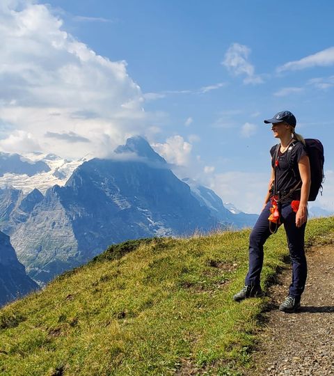 Wanderin steht auf Bergweg und schaut zur grossen Scheidegg. 