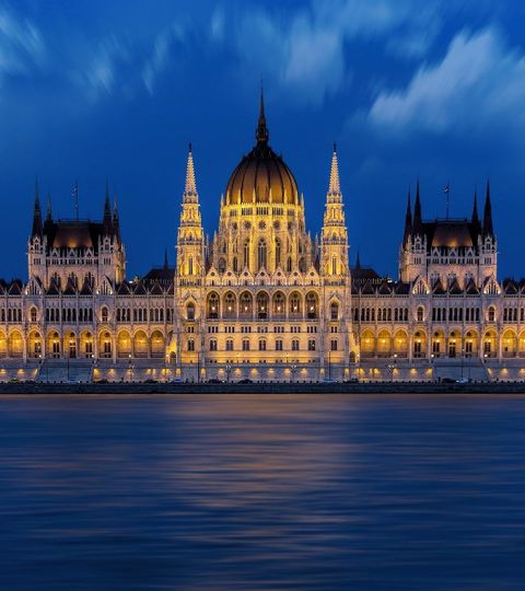 Das Parlementsgebäude in Budapest steht direkt am Ufer der Donau und ist bei Nacht beleuchtet.