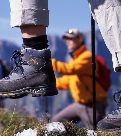 The lower legs of a hiker in his hiking boots and rolled-up trousers can be seen in the centre of the picture. In the background, his three hiking companions can be seen out of focus.