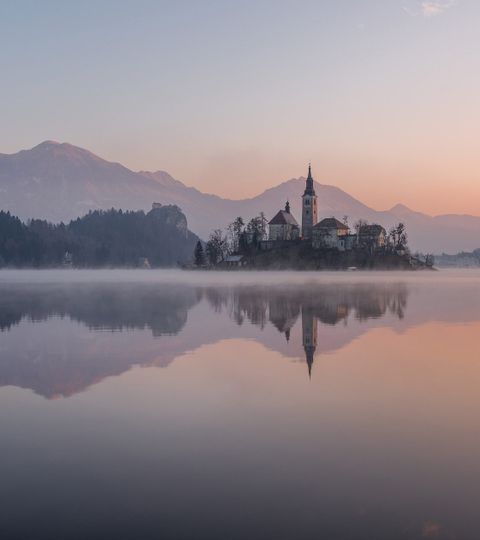 Eine Kirche steht auf einer kleinen Insel auf einem See in den Bergen Sloweniens.