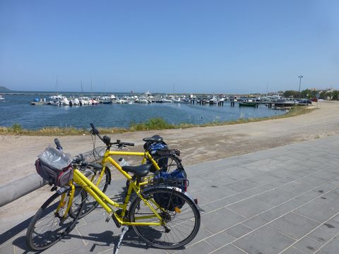 Vorne links sind zwei gelbe Fahrräder am Ufer abgestellt im Hintergrund ein Steg der mit "parkierten" Booten geradezu ubersäht ist. Das ganze natürlich bei Sonnenschein und stahlend blauem Himmel.